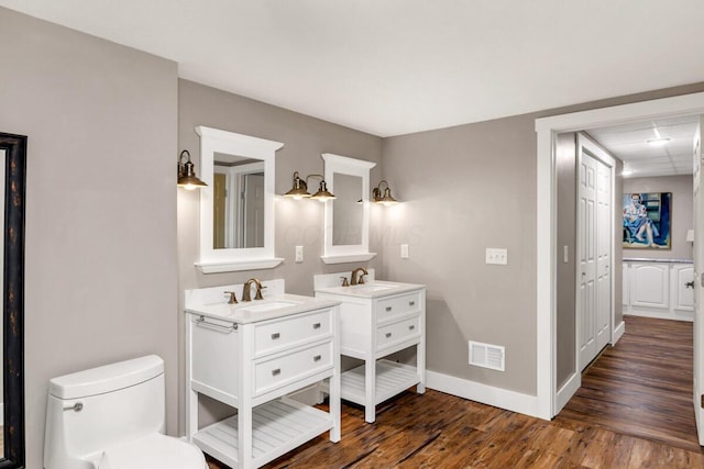 bathroom featuring two vanities, visible vents, toilet, wood finished floors, and baseboards