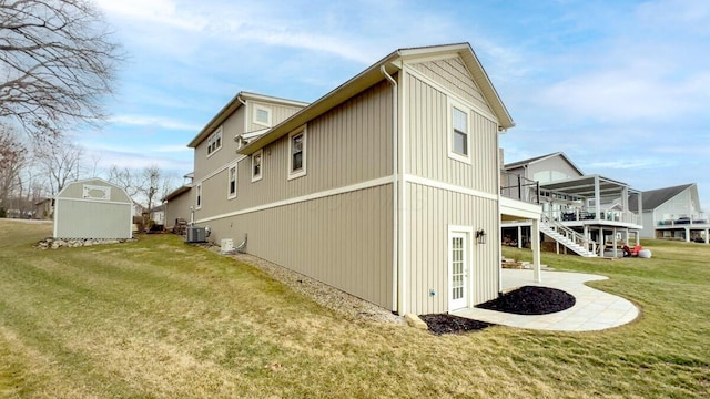 view of property exterior featuring an outbuilding, a lawn, stairway, a shed, and cooling unit