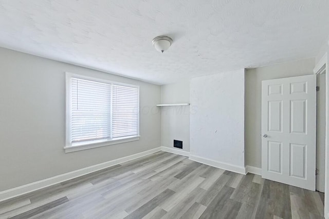 empty room with a textured ceiling, wood finished floors, and baseboards