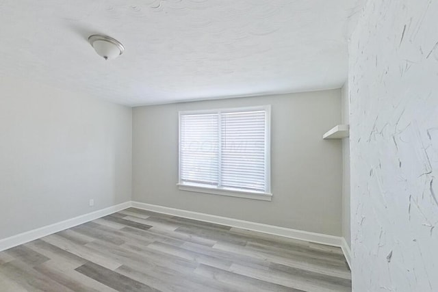 unfurnished room with a textured ceiling, baseboards, and wood finished floors