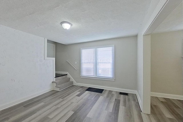 empty room with a textured ceiling, stairway, wood finished floors, and visible vents