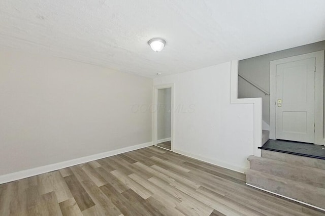 unfurnished room with a textured ceiling, stairway, baseboards, and wood finished floors