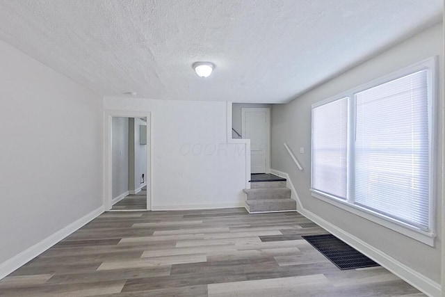 empty room featuring visible vents, a textured ceiling, wood finished floors, baseboards, and stairs