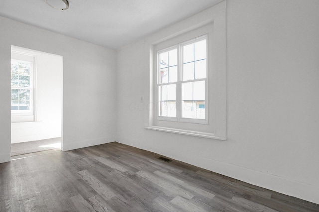 empty room with plenty of natural light, wood finished floors, and visible vents