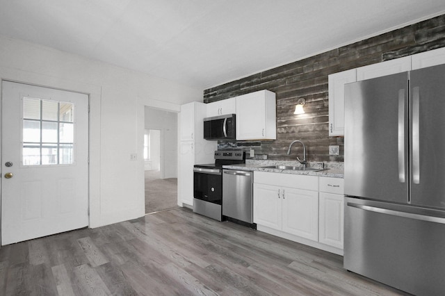 kitchen with appliances with stainless steel finishes, white cabinets, a sink, and wood finished floors