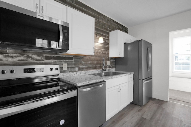 kitchen featuring wood finished floors, a sink, white cabinetry, appliances with stainless steel finishes, and tasteful backsplash