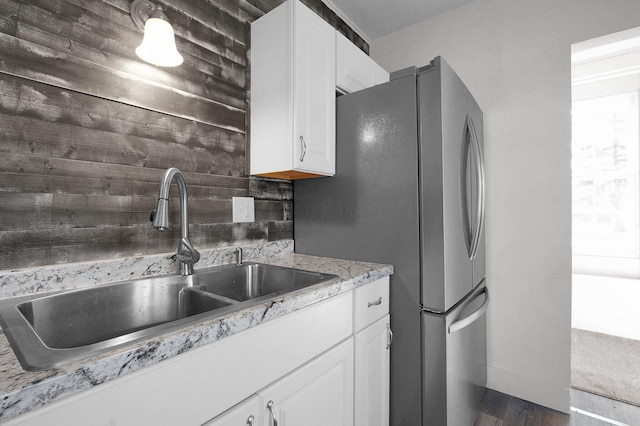 kitchen featuring light stone counters, a sink, white cabinets, freestanding refrigerator, and decorative backsplash