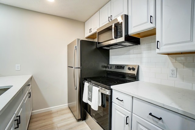 kitchen featuring backsplash, baseboards, light wood-type flooring, stainless steel appliances, and white cabinetry