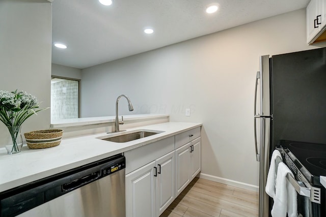 kitchen featuring white cabinets, appliances with stainless steel finishes, light wood-type flooring, and a sink