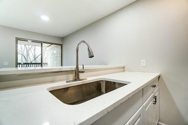 kitchen featuring white cabinetry, light stone counters, recessed lighting, and a sink