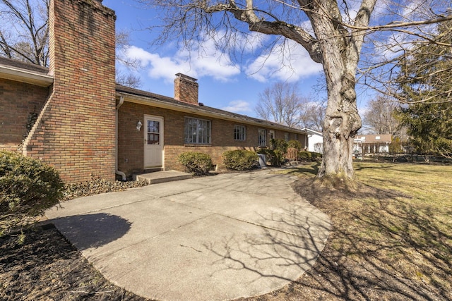 rear view of property with brick siding, a yard, and a chimney