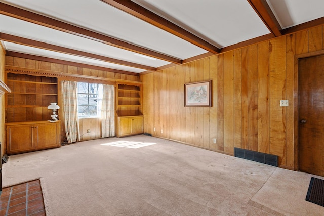 carpeted spare room with wood walls, visible vents, and beamed ceiling