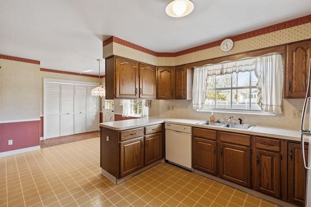 kitchen featuring light countertops, white dishwasher, a sink, and wallpapered walls