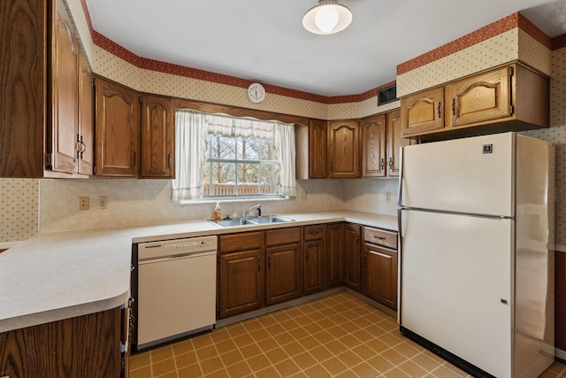 kitchen featuring a sink, white appliances, light countertops, and wallpapered walls