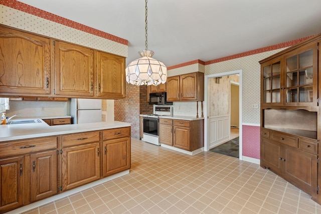 kitchen with light countertops, brown cabinetry, a sink, white appliances, and wallpapered walls