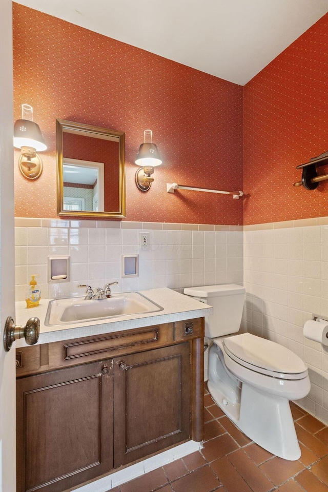 bathroom with wallpapered walls, toilet, a wainscoted wall, vanity, and tile walls