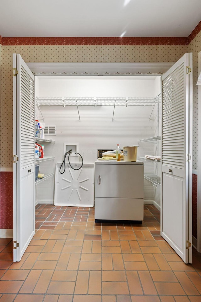 clothes washing area with washer / dryer, visible vents, brick patterned floor, and wallpapered walls