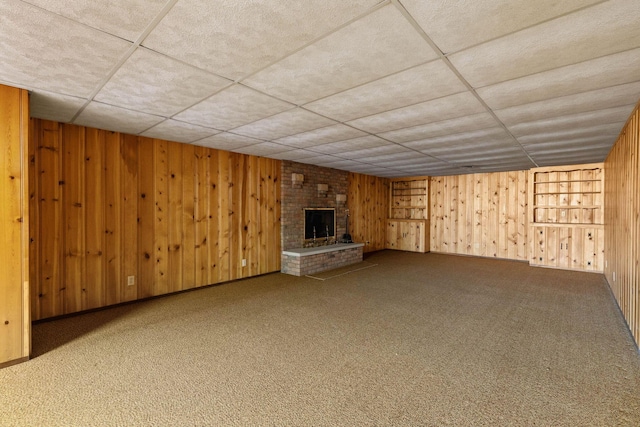 unfurnished living room featuring carpet floors, a brick fireplace, a paneled ceiling, and wooden walls