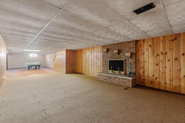 finished basement with carpet floors, a brick fireplace, and wooden walls