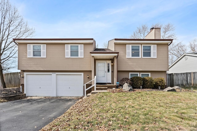 split foyer home featuring aphalt driveway, a chimney, fence, a garage, and a front lawn