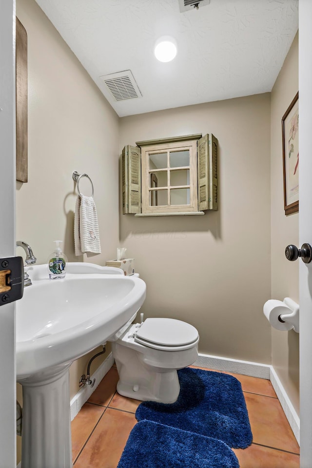 half bathroom with toilet, tile patterned floors, visible vents, and baseboards