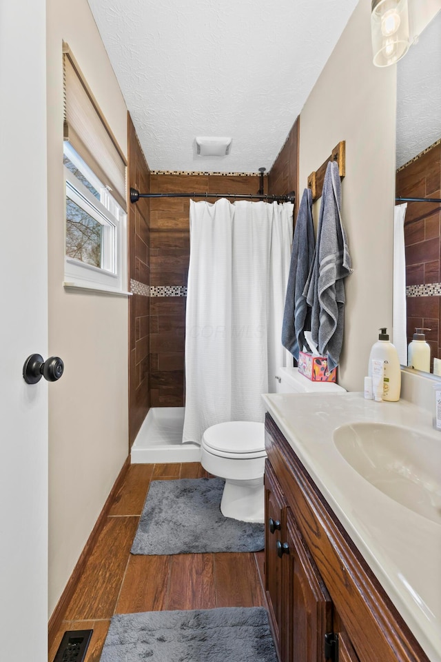 bathroom with visible vents, toilet, wood finished floors, a tile shower, and a textured ceiling