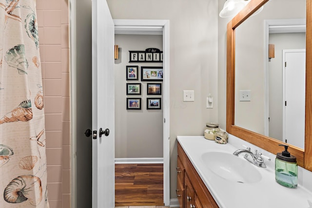 full bath with a shower with shower curtain, baseboards, wood finished floors, and vanity