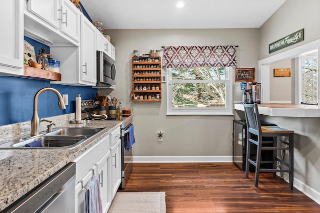 kitchen featuring stainless steel appliances, a sink, white cabinetry, baseboards, and dark wood-style floors