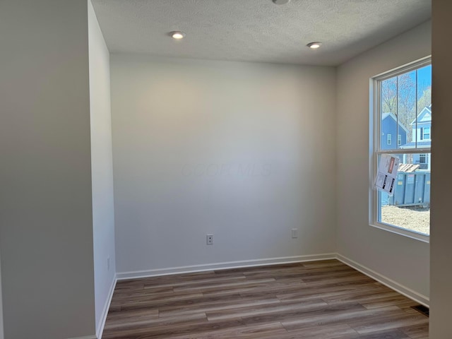 empty room with baseboards, wood finished floors, a textured ceiling, and recessed lighting