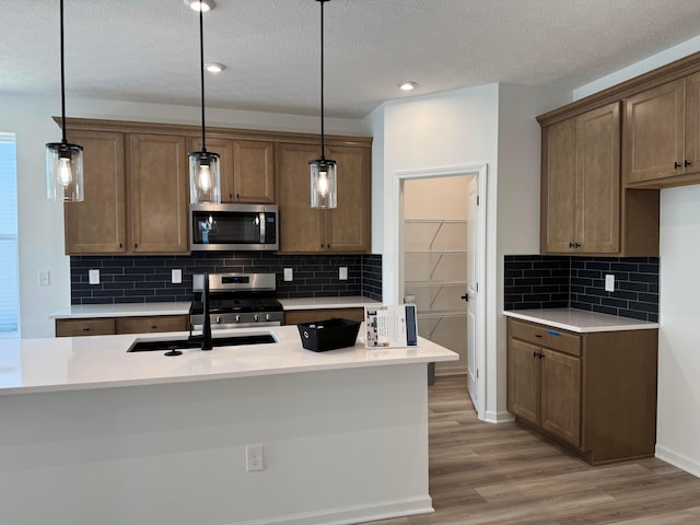kitchen with decorative light fixtures, light wood-style floors, stainless steel appliances, and a sink