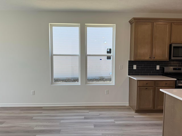 kitchen featuring stainless steel appliances, light wood-type flooring, baseboards, decorative backsplash, and light countertops