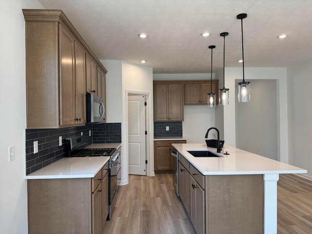 kitchen featuring backsplash, appliances with stainless steel finishes, a sink, and light wood-type flooring