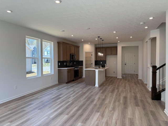 kitchen featuring an island with sink, open floor plan, light wood-style floors, and appliances with stainless steel finishes