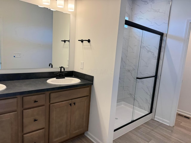 full bathroom featuring wood finished floors, a sink, a marble finish shower, baseboards, and visible vents