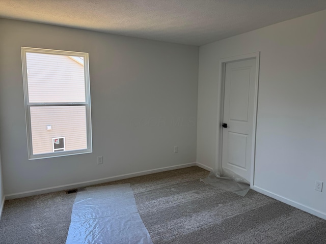 carpeted empty room with baseboards, visible vents, and a textured ceiling