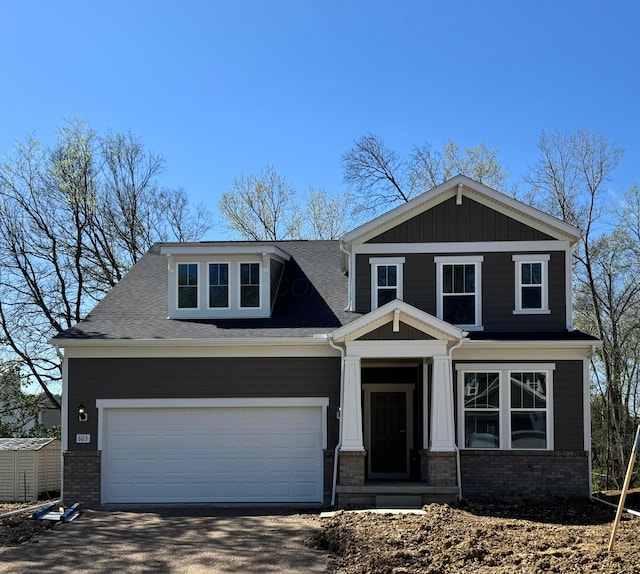 craftsman inspired home featuring a shingled roof, aphalt driveway, and brick siding
