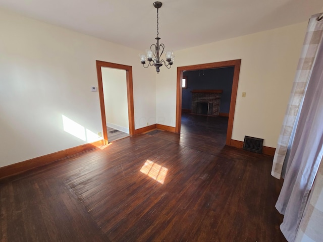 unfurnished dining area featuring a fireplace, a notable chandelier, visible vents, wood finished floors, and baseboards