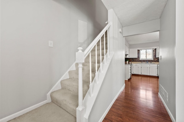 stairway featuring visible vents, wood finished floors, baseboards, and a textured ceiling