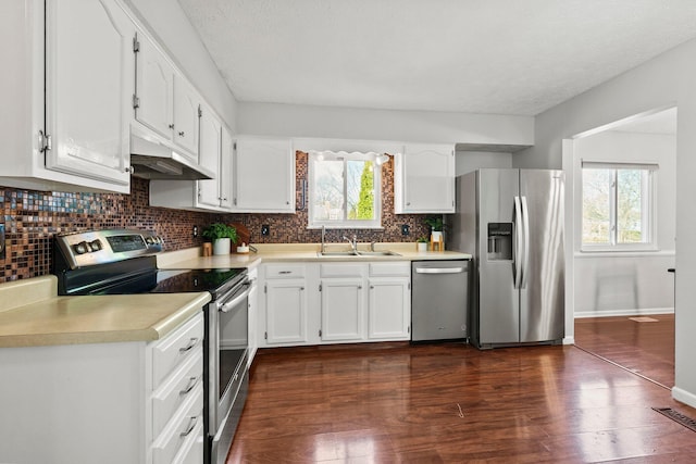 kitchen with backsplash, under cabinet range hood, dark wood finished floors, white cabinets, and stainless steel appliances