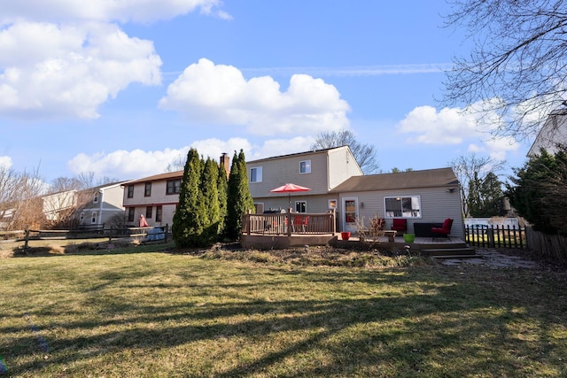 rear view of property featuring a wooden deck, a lawn, and fence