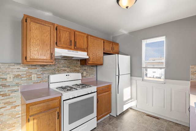 kitchen with white appliances, visible vents, a wainscoted wall, light countertops, and under cabinet range hood