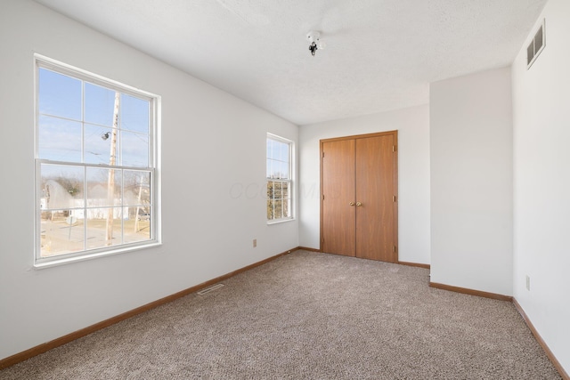 unfurnished bedroom with carpet floors, visible vents, a textured ceiling, and baseboards