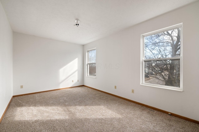 carpeted spare room with visible vents, a textured ceiling, and baseboards