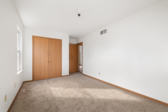 unfurnished bedroom featuring light carpet, a closet, visible vents, and baseboards