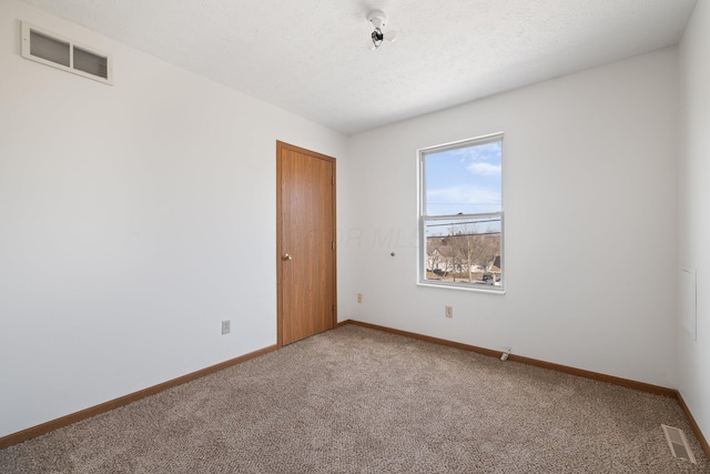 empty room with carpet, visible vents, a textured ceiling, and baseboards