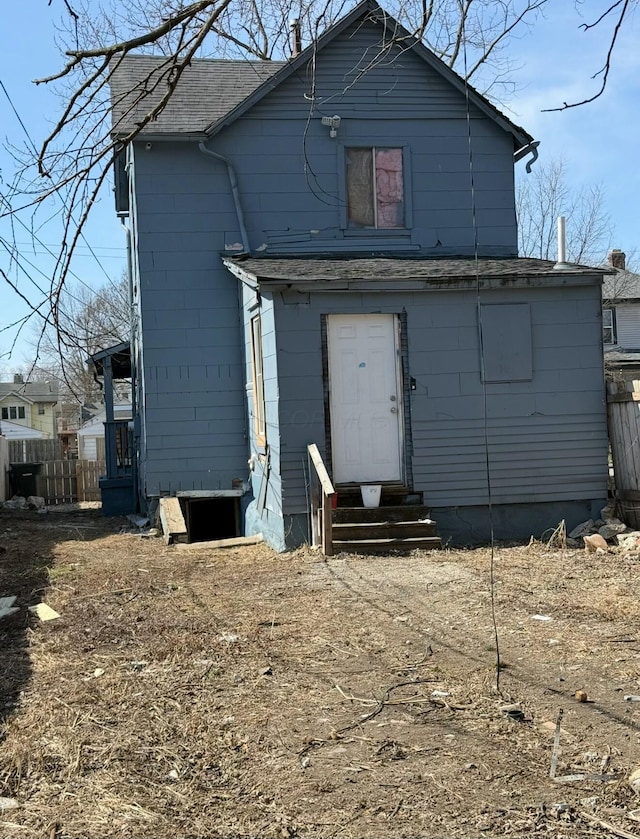 rear view of house with entry steps, a shingled roof, and fence