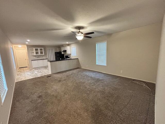 unfurnished living room featuring a textured ceiling, carpet floors, a ceiling fan, and baseboards