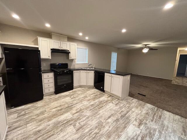 kitchen featuring dark countertops, a peninsula, range hood, black appliances, and white cabinetry