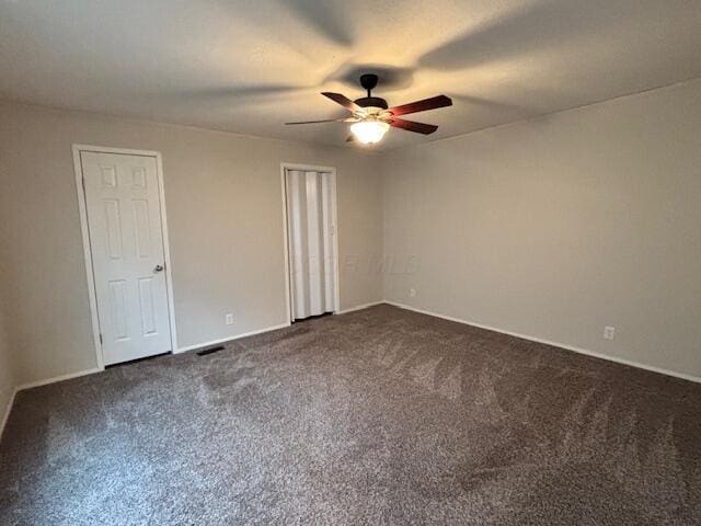 unfurnished bedroom with visible vents, dark colored carpet, and a ceiling fan