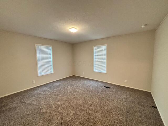 spare room with visible vents, dark carpet, a textured ceiling, and baseboards